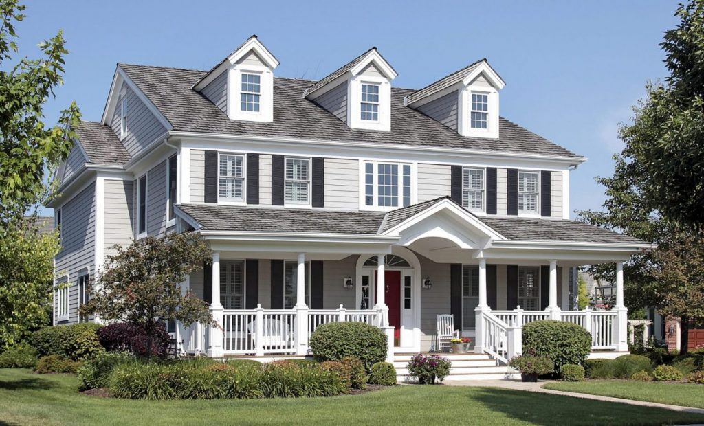 Beautiful two-story home with light gray vinyl siding, black shutters, and a welcoming white porch. Well-maintained lawn and landscaping enhance the curb appeal of this classic house.