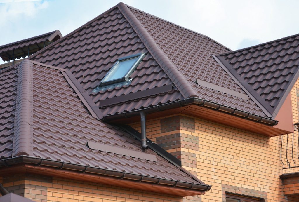 Brown metal roof with a skylight on a brick home in Pasadena, MD. Gutters are visible. Consider roof cleaning in Pasadena MD to maintain curb appeal.